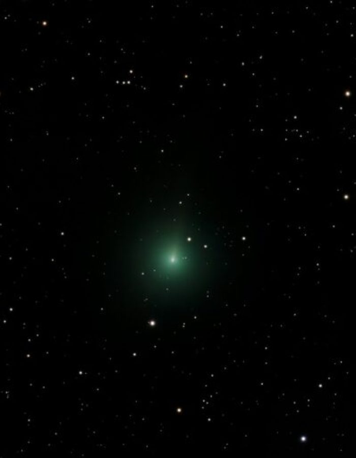 A green comet glows in the starry night sky.